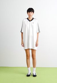 Balta sporta kleita ar īsām piedurknēm, melnu apkakli un trim melnām svītrām uz katras piedurknes. Minimalistisks logo uz krūšdaļas.