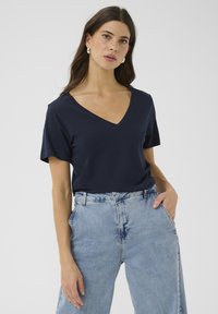 Camiseta de cuello en V de color marino con mangas cortas, hecha de tejido suave. Combinada con unos vaqueros de cintura alta de color azul claro, que muestran un ajuste relajado.