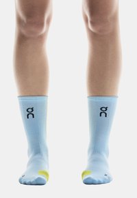 Calze sportive azzurre chiare con logo nero, dettagli gialli sul tallone e sulle punte, e materiale testurizzato progettato per comfort e supporto.