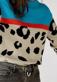 Sweter oversize z górną częścią w pasy w kolorze turkusowym i czerwonym, kremowym dołem z czarnymi cętkami w wzór lamparta, zestawiony ze zdobionym czarnym paskiem.