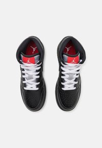 Czarne skórzane trampki z perforowanym czubkiem, białymi sznurowadłami, czerwono-szarymi akcentami wewnątrz oraz logo na języku i bokach.