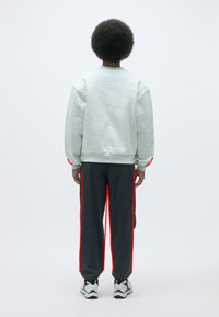 Sudadera gris claro de corte relajado, combinada con pantalones de chándal gris oscuro con franjas laterales rojas. Las zapatillas completan el conjunto.