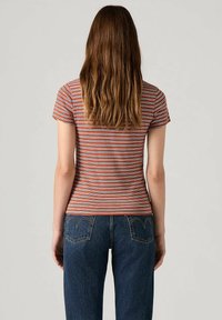 Top ajustado de manga corta con rayas horizontales en naranja y gris; combinado con jeans oscuros de cintura alta que tienen bolsillos en la parte posterior.