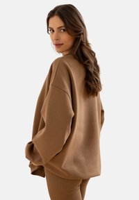 Brązowy, oversize'owy sweter z miękkiego materiału, z opadającymi ramionami i luźnym krojem. Noszony z pasującymi legginsami.