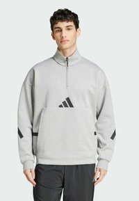 Grå sweatshirt med hög krage och halvmatch, med svarta adidas-logotypdetaljer på bröstet och ärmarna. Mjuk, strukturerad tyg.