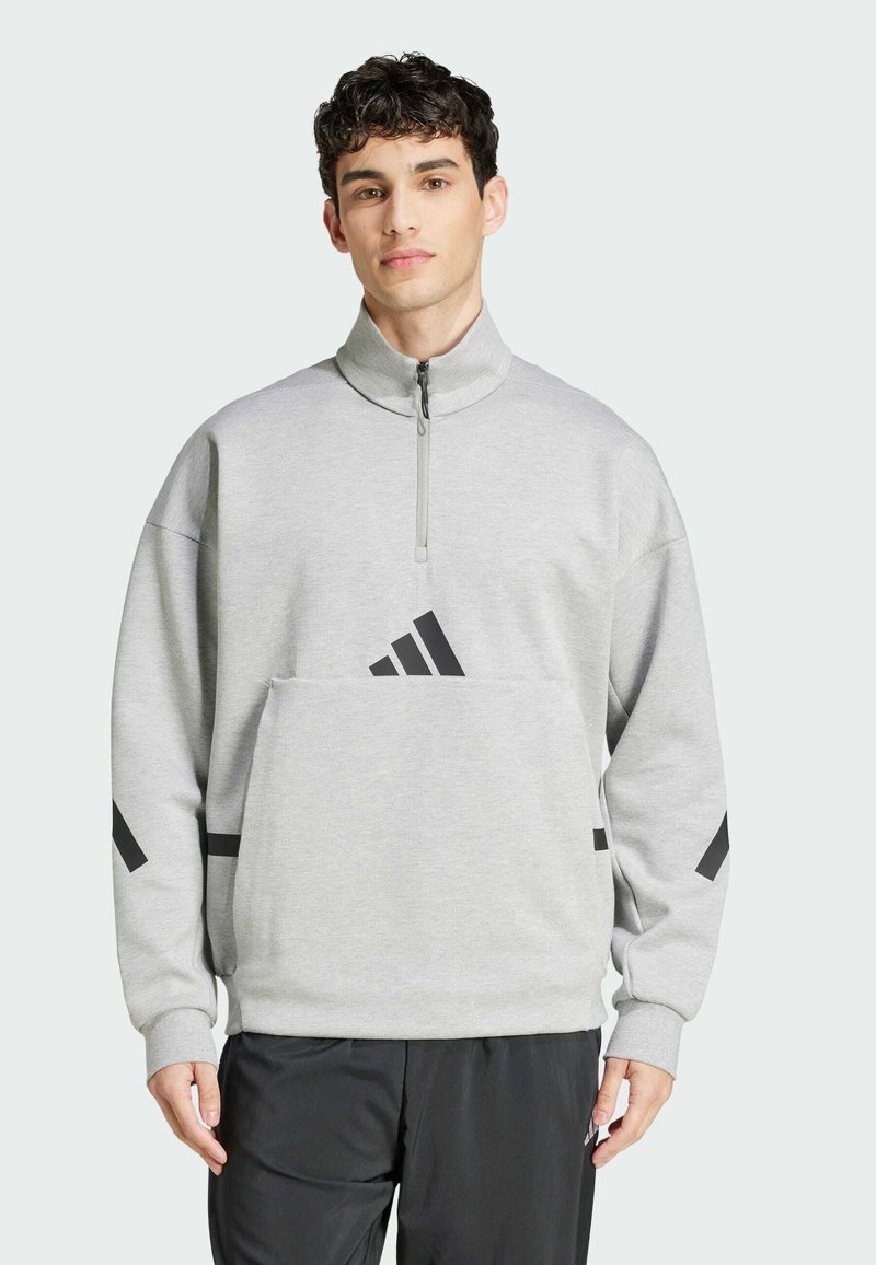 Grå sweatshirt med hög krage och halvmatch, med svarta adidas-logotypdetaljer på bröstet och ärmarna. Mjuk, strukturerad tyg.