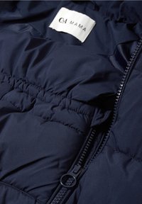 Gros plan d'une veste matelassée bleu marine avec une fermeture éclair et une étiquette en tissu blanc affichant "C&A MAMA."