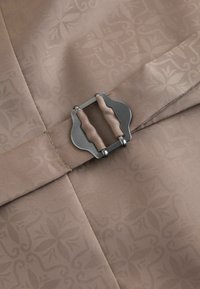 Tela marrón claro con un sutil patrón floral que presenta una hebilla de doble lengüeta cubierta con tela a juego, sujetada de forma segura.