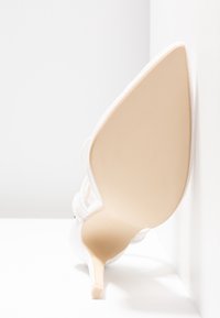 Chaussure stiletto blanche à bout pointu avec des brides texturées, affichée semelle vers le haut sur un fond blanc en coin.