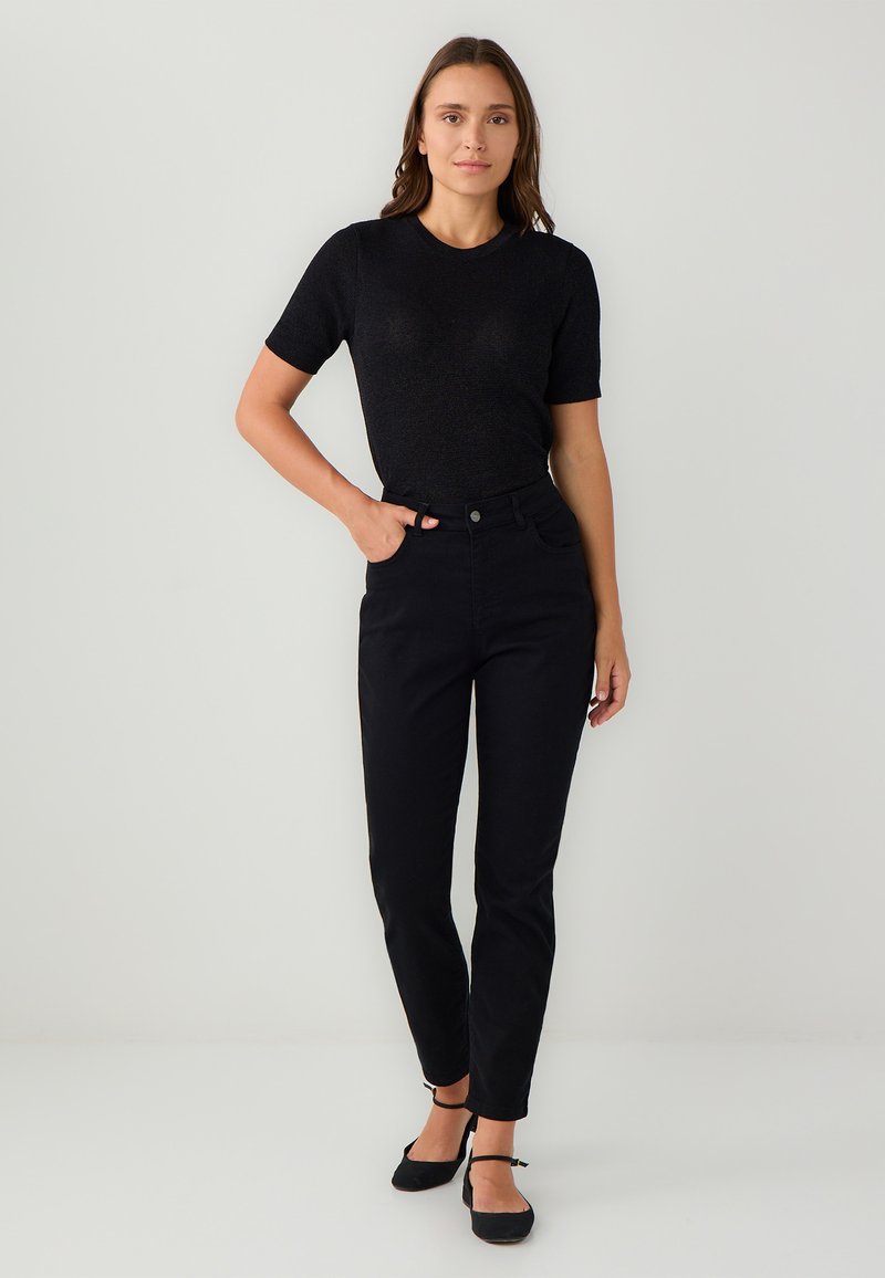 Czarna koszula z krótkim rękawem o teksturowanym wykończeniu, w połączeniu z czarnymi spodniami z wysokim stanem i czarnymi płaskimi sandałami na paski. Prosty i dopasowany krój.