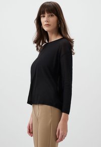 Zwarte, lichte langemouwtop met een ronde halslijn en zijsplitten, gecombineerd met beige op maat gemaakte broek, die een gladde textuur toont.