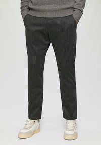 Zwarte broek met streepjes in een slim fit, gemaakt van een gestructureerde stof. Gecombineerd met lichtgekleurde sneakers met een rubberen zool.