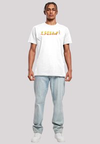 Hvit bomulls t-skjorte med et flerfarget tegneseriefigur grafikk. Modellen kombinerer den med lyseblå denimjeans og hvite joggesko.