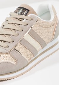 Basket beige et or Versace Jeans avec tissu pailleté texturé, détails en daim, lacets beiges et logo de la marque sur la languette et le côté.
