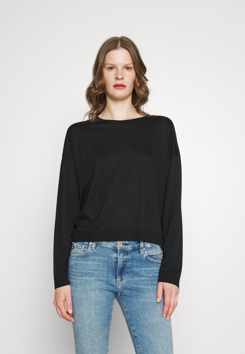 Svart langermet topp med avslappet passform, rund halslinje og myk tekstur, sammen med lyseblå denimbukser.