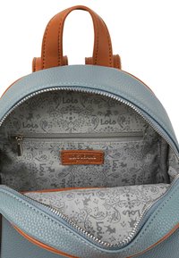 Mochila azul texturizada con detalles en cuero marrón. El interior cuenta con un forro gris claro con un patrón y un bolsillo con cremallera para mayor organización.