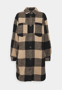 Rutig jacka med svart och beige mönster, tillverkad av texturerat tyg. Har en krage, två bröstfickor och framknappar.