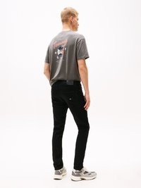Grijze T-shirt met een kleurrijk grafisch ontwerp op de achterkant, gecombineerd met zwarte broeken en grijze sneakers; casual pasvorm en eenvoudige styling.