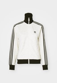 Bílá sportovní bunda na zip s černými detaily, vybavená vysokým límcem, třemi černými pruhy na rukávech a texturovaným vzorem po celé látce.