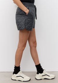 Shorts gris matelassés avec une taille à cordon, des poches latérales et un ourlet arrondi, associés à des baskets blanches et noires et des chaussettes côtel�ées noires.