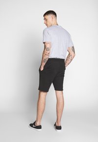 Camiseta gris de manga corta, combinada con pantalones cortos negros. Los pantalones cortos tienen una textura suave y una cinturilla elástica.