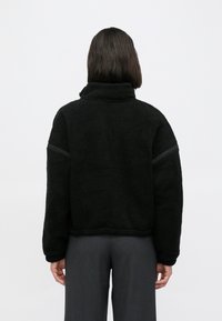 Giacca in pile nera con collo alto, superficie strutturata e sottili strisce sulle spalle, caratterizzata da una vestibilità comoda e orlo costellato.