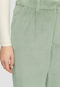 Lichtgroene corduroybroek met ribbeltextuur, een knoopsluiting en zijzakken, gedragen met een longsleeve top.