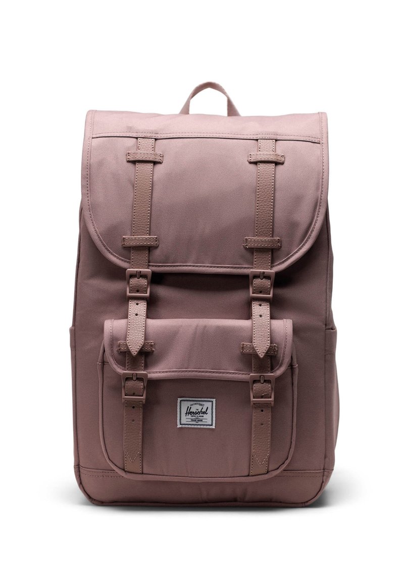 Vaaleanpunainen reppu, jossa on kanvaalipinta, yläläppä, kaksi etutaskua ja säädettävät hihnat, etupuolella oleva logotägi.