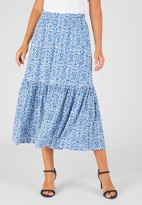 Gonna maxi a fantasia blu e bianca con design a campana, vita elastica e orlo arricciato; abbinata a sandali neri con cinturini.