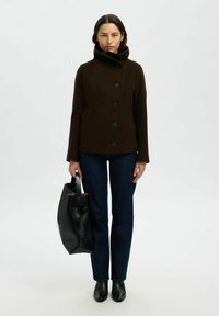 Giacca in misto lana marrone con colletto alto e chiusure a bottone, abbinata a jeans scuri e una borsa in pelle nera. Tessuto liscio, vestibilità sartoriale.