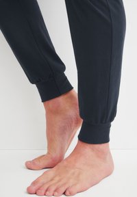 Zwarte katoenen joggers met elastische boorden, met blote voeten zichtbaar. De stof lijkt zacht en lichtgewicht, met een gladde textuur.