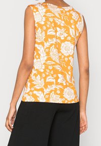 Bezramenný top v jasně oranžové barvě s bílými květinovými vzory. Má kulatý výstřih a přiléhavý střih, vyrobený z měkké bavlněné tkaniny.
