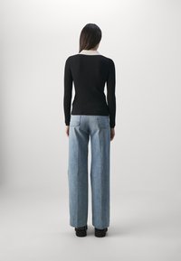 Haut noir à manches longues côtelé avec un col blanc contrastant, assorti à un jean large bleu clair et des chaussures plateformes noires.