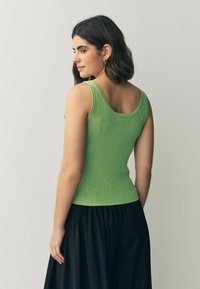 Débardeur vert à côtes avec un col en scoop et une coupe slim, associé à une jupe noire fluide. Présente un tissu texturé et une silhouette ajustée.