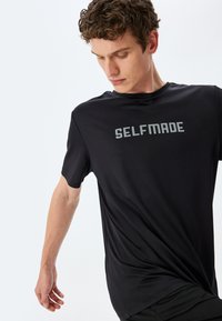 Czarny sportowy t-shirt z okrągłym dekoltem, krótkimi rękawami i wyrazistym, szarym napisem "SELFMADE". Miękka, lekka tkanina o teksturowanym wykończeniu.