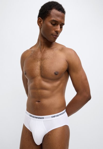 Caleçon blanc en coton avec une ceinture noire à logo, offrant une coupe ajustée et une texture lisse, porté par un mannequin homme.