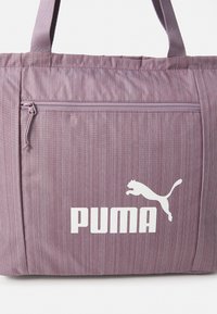 Lila gestreifte Tragetasche aus Stoff, mit einer vorderen Reißverschlusstasche, großem weißen "PUMA"-Logo und einer springenden Katzensilhouette.