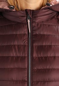 Donkerrode pufferjas met een doorgestikt ontwerp, hoge kraag met een roze capuchon, volledige ritssluiting en een glanzende, gladde textuur.