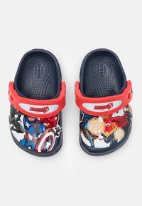 Des Crocs bleu marine avec une sangle rouge, présentant des super-héros Marvel colorés sur la surface supérieure. Texture lisse avec des trous de ventilation.
