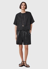 Svart kort topp i en texturerad tyg, kombinerad med högmidjade svarta lädershorts och svarta sandaler med remmar, minimal smyckesstil.