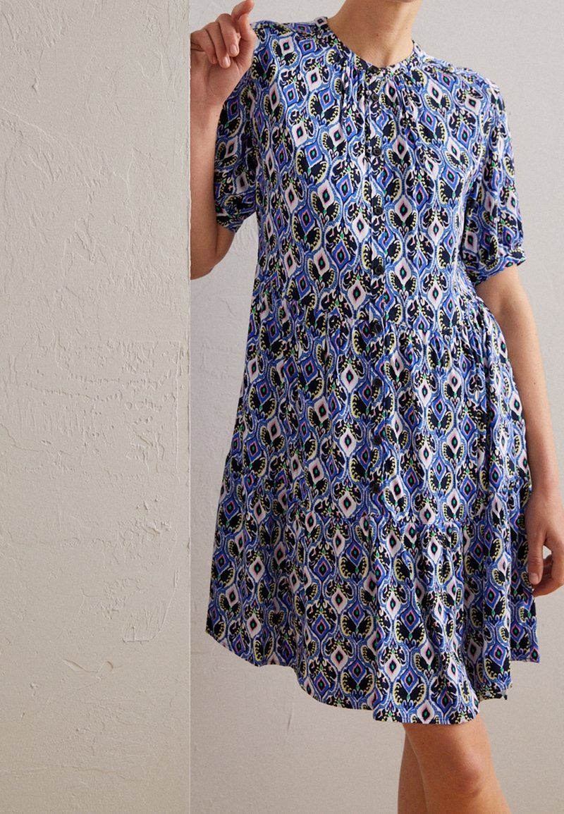 Vestido azul de manga corta con un patrón geométrico multicolor, recogido en el escote y la cintura, hecho de una tela ligera.