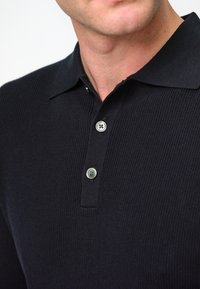 Schwarzes, geripptes Poloshirt mit Kragen und zwei-Knopf-Leiste, ausgestattet mit silberfarbenen Knöpfen und einem strukturierten Stoff.