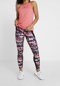 Różowy sportowy top bez rękawów w połączeniu z czarnymi legginsami z różowo-białym abstrakcyjnym wzorem. Całość dopełniają białe trampki.