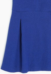 Une jupe en tissu bleu avec un motif texturé, présentant des plis au bas et une taille lisse. Le tissu a une surface légèrement en relief.