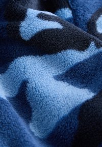 Tissu polaire doux avec une texture en relief dans un motif camouflage bleu foncé et bleu clair, montrant des plis et des ombres.