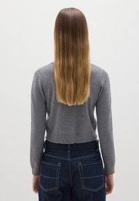 Suéter gris de punto con un diseño cropped y mangas largas, combinado con jeans de mezclilla oscuros que tienen costuras en contraste y bolsillos traseros.