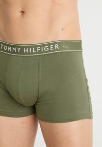 Olijfgroene boxershorts voor heren met een witte elastische tailleband waarop het logo 'TOMMY HILFIGER' staat. Zachte, rekbare stof met een gladde textuur.