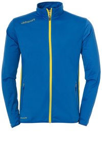 Blaue Jacke mit hohem Kragen, durchgehendem gelben Reißverschluss, Seitentaschen und gelbem Markenlogo auf der linken Brust. Glatte Textur.