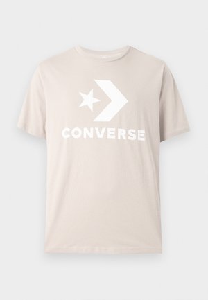 Smėlio spalvos medvilniniai marškinėliai su balto žvaigždės ir rodyklės dizainu, priekyje ryškiai išraižytu užrašu „CONVERSE“ storu šriftu.