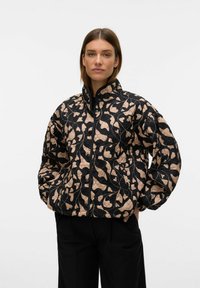 Gequilted jas in zwart en beige met een abstracte bladerenpatroon. Voorzien van een hoge kraag en een ritssluiting aan de voorkant, met oversized mouwen voor extra comfort.